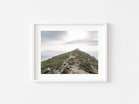 A framed landscape photograph of a grassy mountain peak path of Ceann Sibeal under a cloudy sky, displayed on a clean white wall.