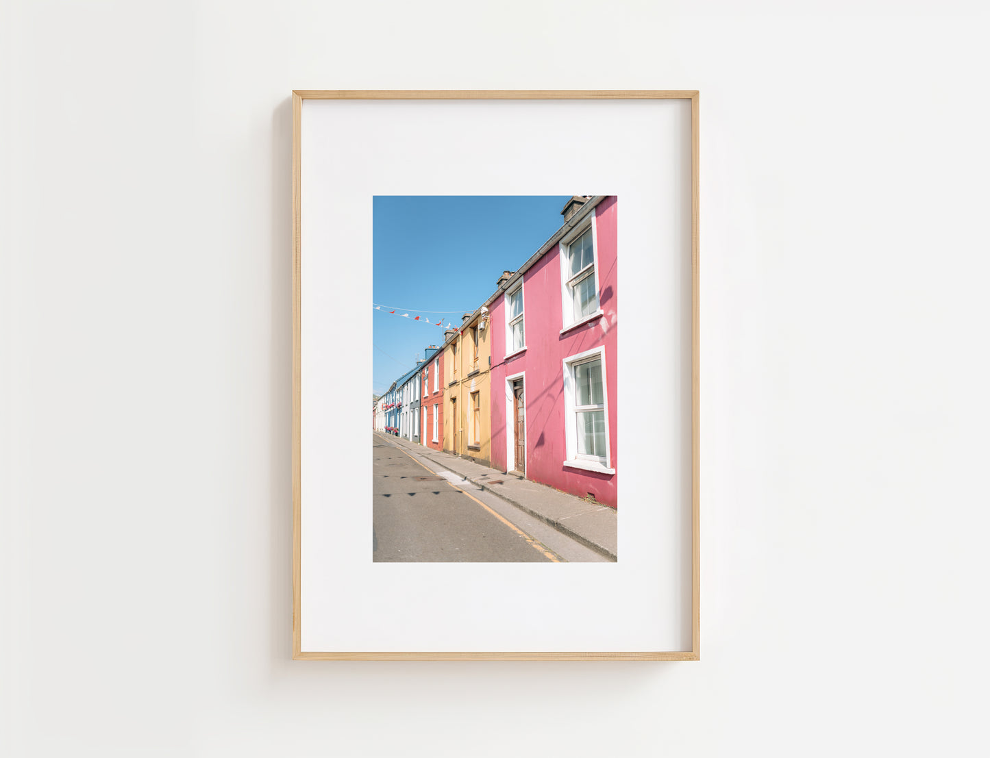 A framed art print featuring a photograph of colorful row houses lining a street under a clear blue sky, displayed on a clean white wall.